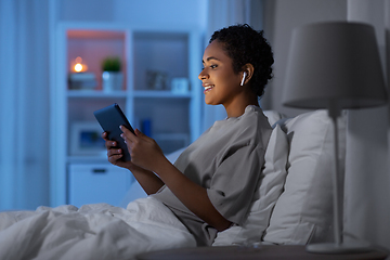 Image showing woman with tablet pc in earphones in bed at night