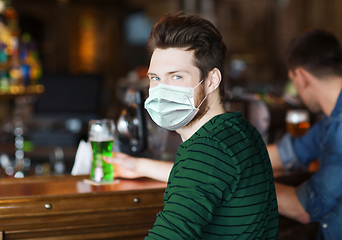 Image showing young man in mask drinking green beer at bar