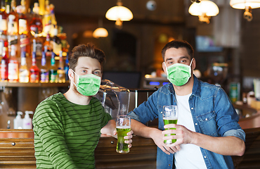 Image showing male friends in masks drinking green beer at bar