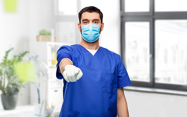 Image showing male doctor in blue scrubs and mask points finger