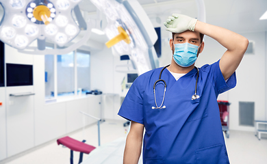 Image showing tired male doctor in blue uniform, mask and gloves