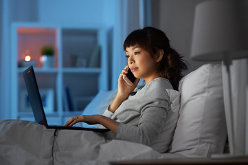 Image showing woman with laptop calling on phone in bed at night