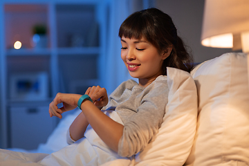 Image showing asian woman with health tracker in bed at night