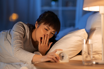 Image showing asian woman with clock yawning in bed at night