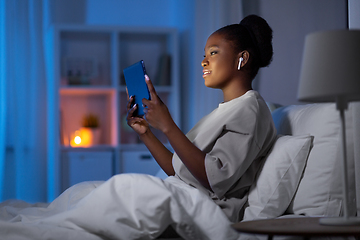 Image showing woman with tablet pc and earphones in bed at night