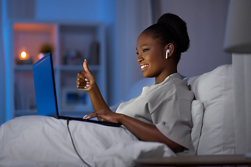 Image showing woman with laptop and earphones in bed at night