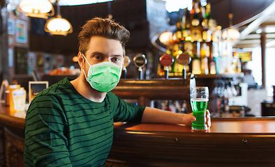 Image showing young man in mask drinking green beer at bar