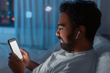 Image showing man with smartphone and earphones in bed at night