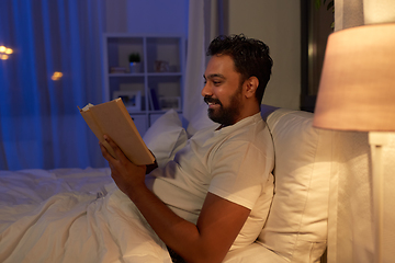 Image showing happy indian man reading book in bed at night