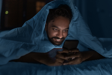 Image showing indian man with smartphone in bed at home at night