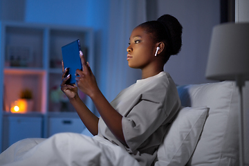 Image showing woman with tablet pc and earphones in bed at night