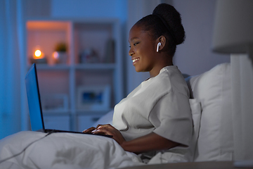 Image showing woman with laptop and earphones in bed at night