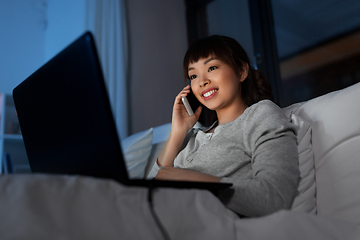 Image showing woman with laptop calling on phone in bed at night
