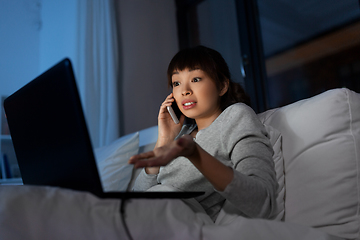 Image showing woman with laptop calling on phone in bed at night