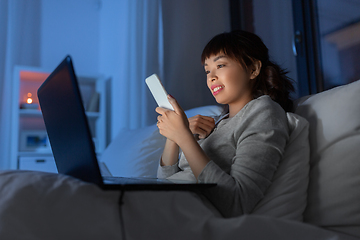 Image showing asian woman with smartphone in bed at night