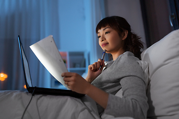 Image showing asian woman with laptop and papers in bed at night