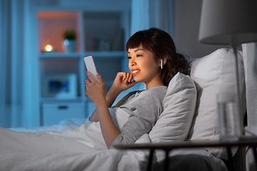 Image showing woman with phone and earphones in bed at night