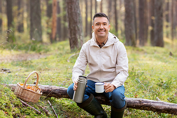 Image showing man with basket of mushrooms drinks tea in forest