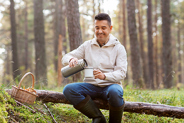 Image showing man with basket of mushrooms drinks tea in forest