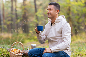 Image showing man with basket of mushrooms drinks tea in forest