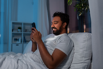 Image showing indian man with smartphone in bed at home at night