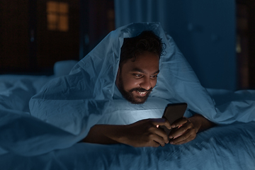 Image showing indian man with smartphone in bed at home at night