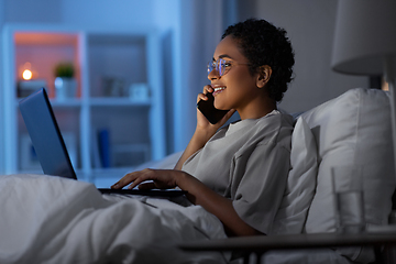 Image showing woman with laptop calling on phone in bed at night