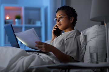Image showing woman with papers calling on phone in bed at night
