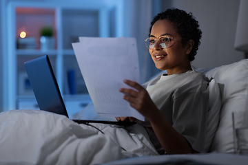 Image showing woman with laptop and papers in bed at night