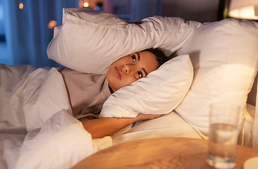 Image showing angry african woman lying in bed and closing ears