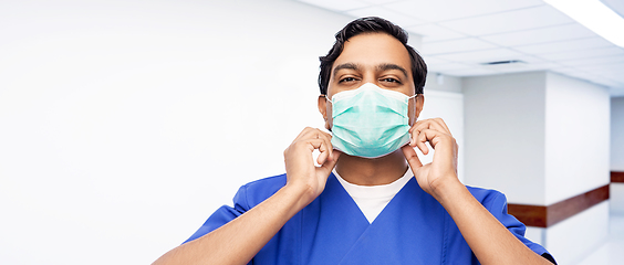 Image showing indian male doctor in blue uniform putting mask on