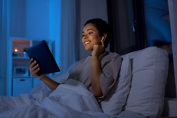 Image showing woman with tablet pc in earphones in bed at night