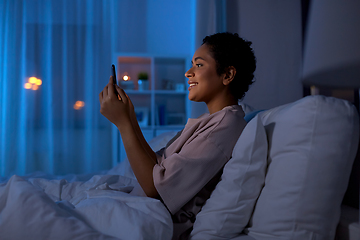 Image showing woman with smartphone in bed at home at night