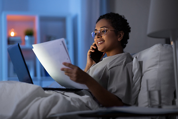 Image showing woman with papers calling on phone in bed at night