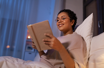 Image showing smiling young woman reading book in bed at home