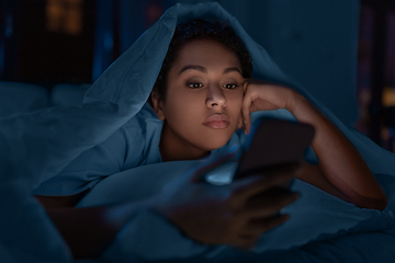 Image showing woman with smartphone under duvet in bed at night