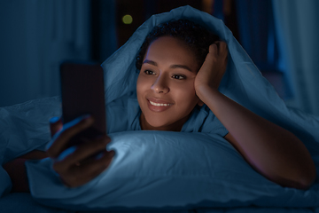 Image showing woman with smartphone under duvet in bed at night