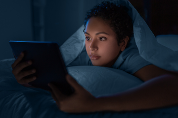 Image showing woman with tablet pc under duvet in bed at night