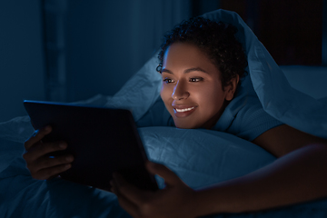 Image showing woman with tablet pc under duvet in bed at night