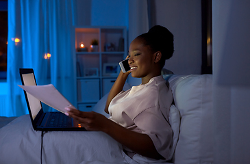 Image showing woman with papers calling on phone in bed at night