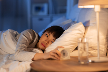 Image showing asian woman with clock lying in bed at night