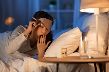 Image showing asian woman with clock yawning in bed at night