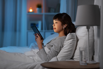 Image showing woman with tablet pc in earphones in bed at night