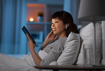 Image showing woman with tablet pc in earphones in bed at night