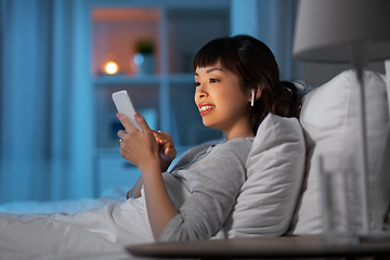 Image showing woman with phone and earphones in bed at night