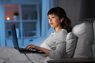 Image showing woman with laptop and earphones in bed at night