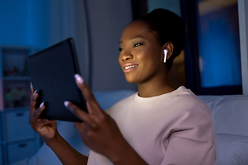 Image showing woman with tablet pc in earphones in bed at night