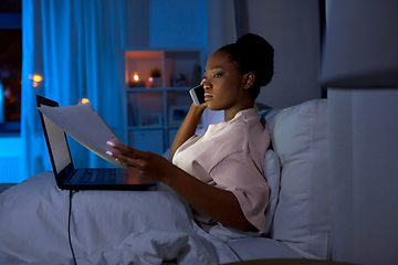 Image showing woman with papers calling on phone in bed at night