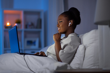 Image showing woman with laptop and earphones in bed at night