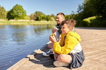 Image showing father and son eating sandwiches on river berth